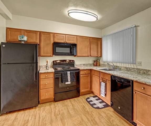 A large kitchen with black appliances, marble countertops with ample space, and spacious wooden cabinets with decorations at Montclair Apartment Homes.