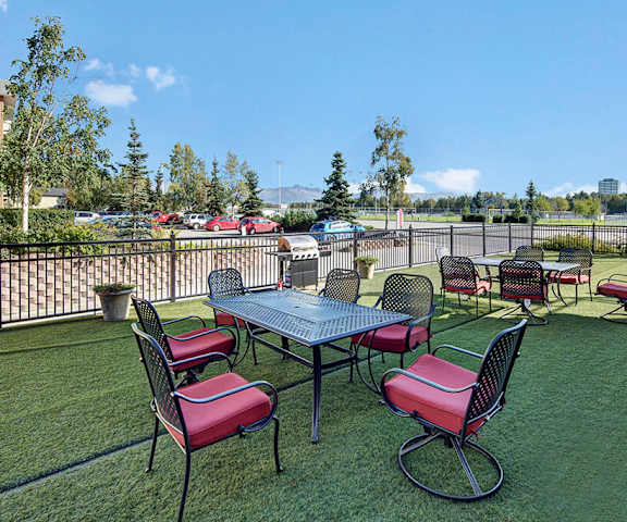 The grilling area with tables, chairs with red cushions, and a grill on a grassy area by the parking lot of Park Plaza II Apartments. 
