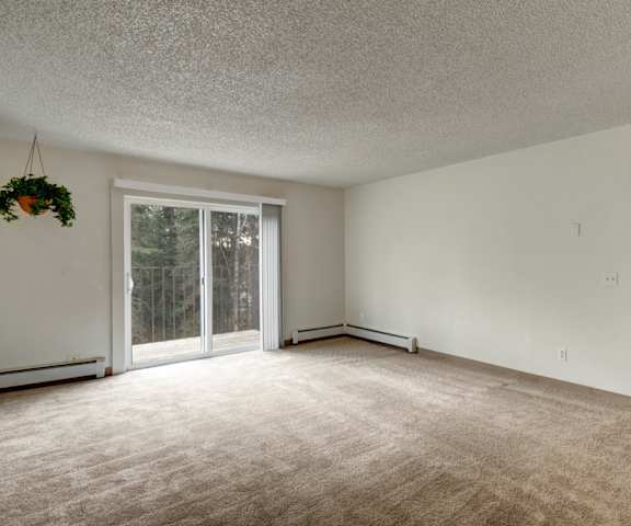 A large empty living room with carpeting and a door to the balcony at Quiet Creek Apartments. 