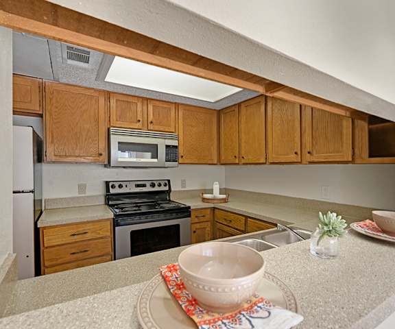 A spacious kitchen with black appliances, marble countertops with lots of room, and wooden cabinets with two places set at the bar at Summertree Place Residences. 