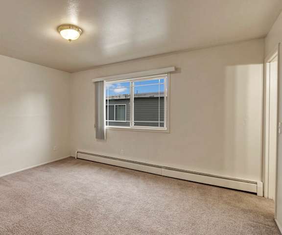 A large, empty carpeted bedroom with overhead lighting and a window at the Village at Calais Apartment Homes. 