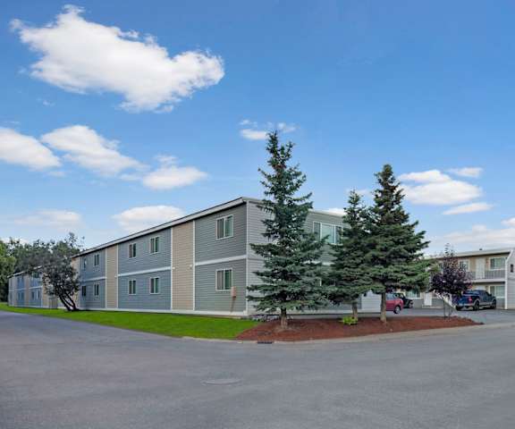 The exterior of the light blue and tan apartments and their parking lots surrounded by trees at the Village at Calais Apartment Homes. 