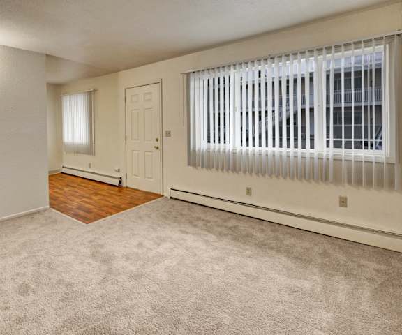 A view of the large empty living room with a window and the door at the Village at Calais Apartment Homes. 