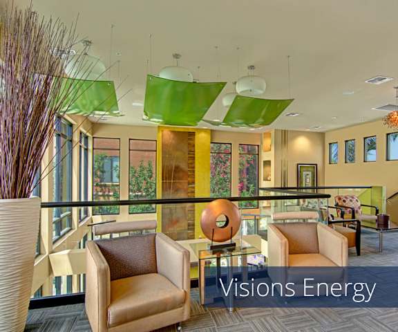 The amazing green and yellow themed resident lounge with couches, decorations, large windows, unique overhead lighting, plush chairs, and coffee tables at Visions Apartment Homes. 