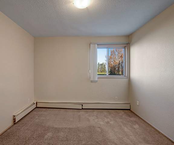 An empty bedroom with a window and carpet at Cedar Gardens Apartments. 