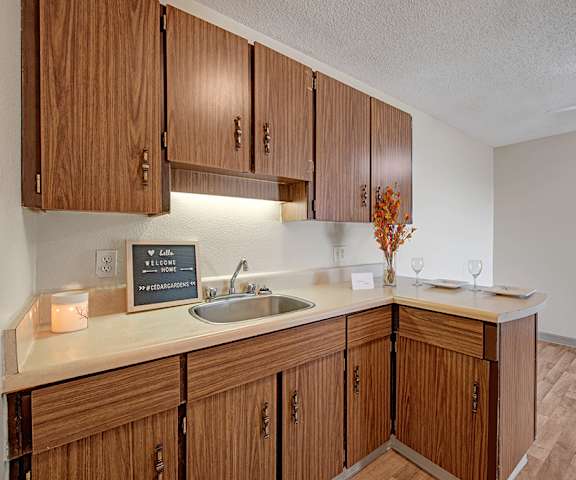 A kitchen with light brown wood cabinets and place settings at Cedar Gardens Apartments. 