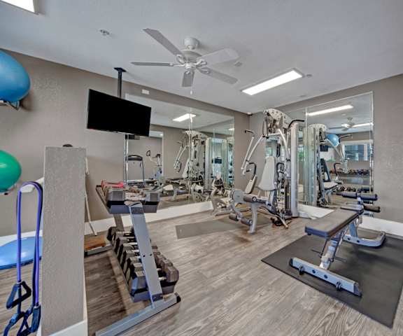 A spacious gym with cardio machines, exercise balls, windows, TVs, benches, and weights at Summit Point Apartment Homes. 