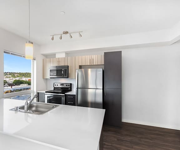A large, bright, modern kitchen with stainless steel appliances, white countertops, lighting fixtures, and large black wooden cabinets at Vive Apartment Homes. 