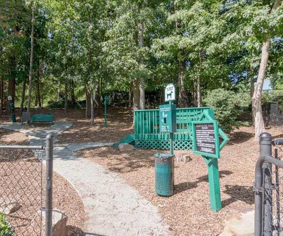 A green sign with a white arrow pointing to the right is on a post in a park.