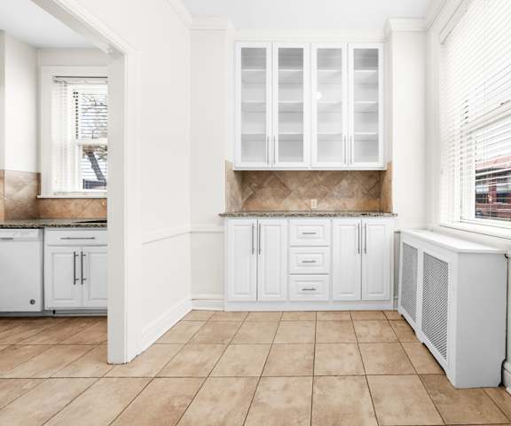A kitchen with white cabinets and a window with blinds.