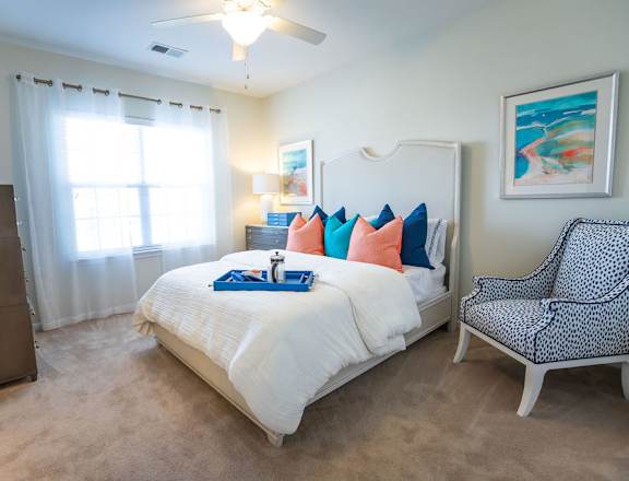 A bedroom with a bed, chair, and a painting on the wall.