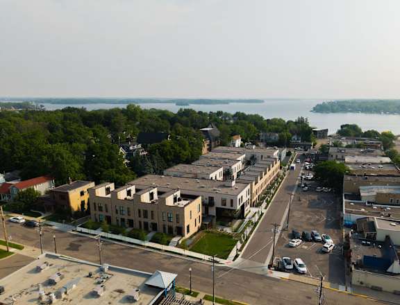 A view of a town with a parking lot in the foreground and a body of water in the background.
