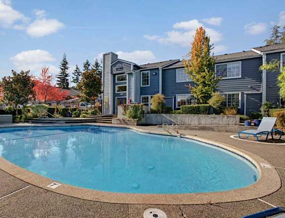 A swimming pool in front of a building with trees in the background.
