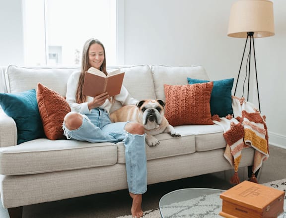 a girl sitting on a couch reading a book with her dog