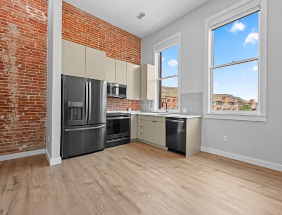 A kitchen with a brick wall and wooden floors. at The Avenue Lofts Golden Apartments, Golden 80401