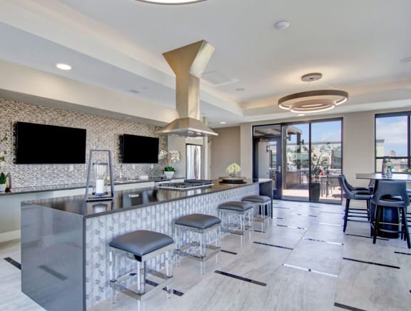 The community kitchen with a coffee machine, toaster, fridge, marble counters, and barstool chairs at Gatsby Apartments. 