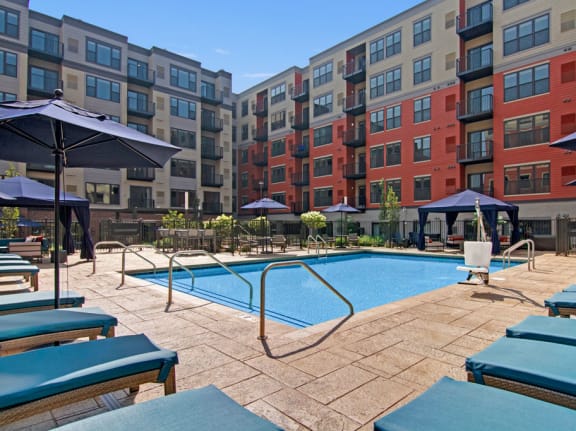 The turquoise outdoor pool with pool chairs, tables, and chairs at Gatsby Apartments. 