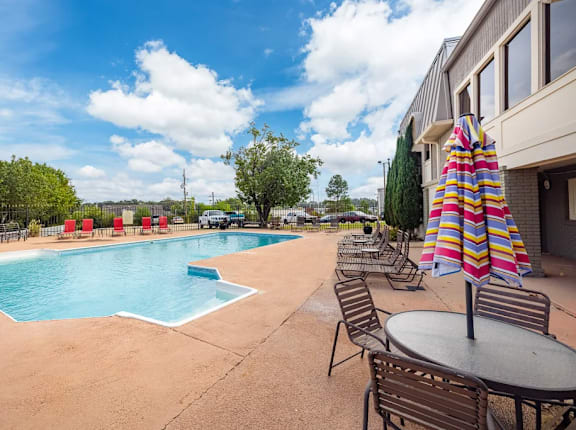 A pool area with chairs and a table with an umbrella.