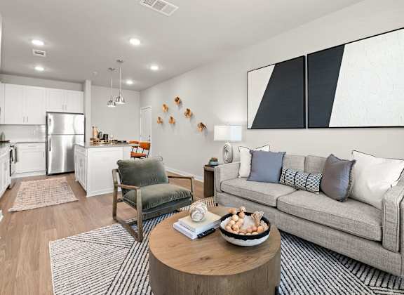 A modern living room with a grey couch, a wooden coffee table, and a kitchen area in the background.