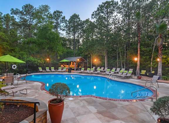 A pool surrounded by trees and lounge chairs.