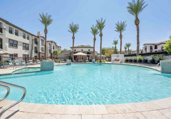 A large swimming pool surrounded by palm trees and apartment buildings.