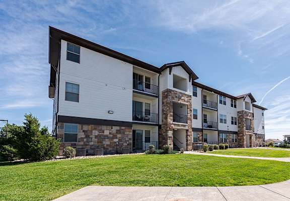 A modern apartment building with a stone facade and a well-maintained lawn in front at Vistas at Jackson Creek, Monument, CO