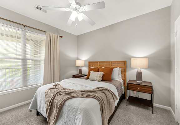 A bedroom with a bed, two lamps, and a ceiling fan.
