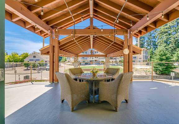 A wooden pergola with a table and chairs is set up outside.