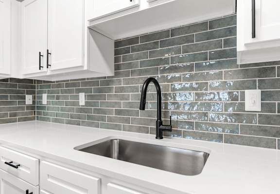 A kitchen with a sink and a grey tile backsplash.