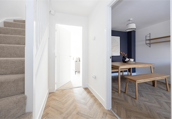 A hallway with a staircase on the left and a table with chairs on the right.