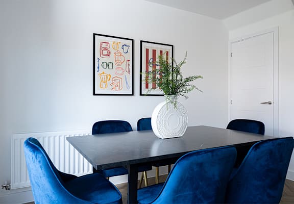 A dining table with blue chairs and two framed pictures on the wall.