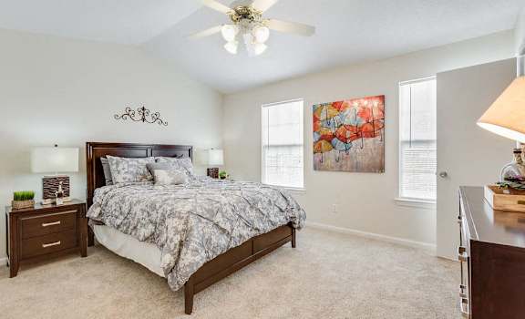 A bedroom with a large bed, a ceiling fan, and a painting on the wall.