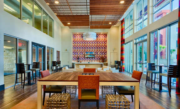 a large table with chairs in a large room with large windows a swimming pool with lounge chairs and umbrellas in front of an apartment building at Elevation on Central Apartments, Phoenix, AZ, 85012
