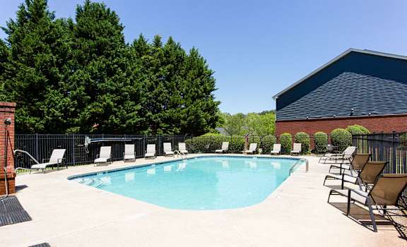 A pool surrounded by trees and chairs at Ballantyne Commons of Stockbridge Apartments, Stockbridge, Georgia