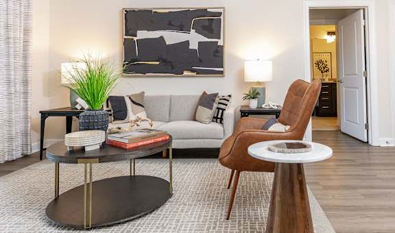 A living room with a grey couch, a wooden chair, a coffee table, and a painting on the wall.