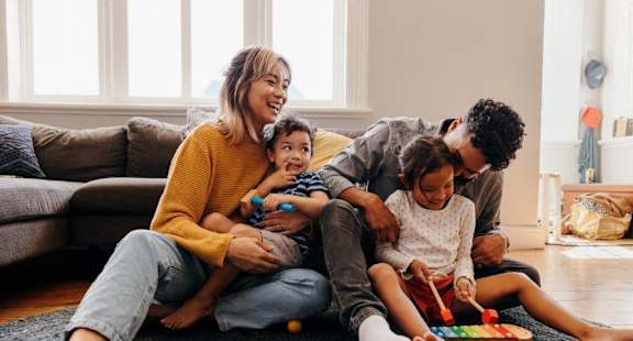 A family of four is playing with toys on the floor in their living room.