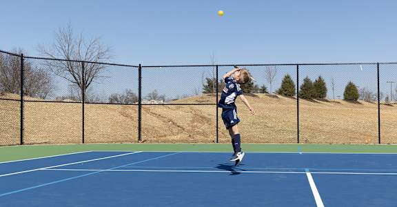 a young boy jumping to hit a tennis ball on a tennis court