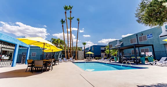 A pool area with a yellow umbrella and a blue building in the background.