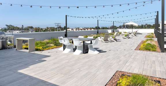 A patio with white chairs and tables is decorated with string lights.