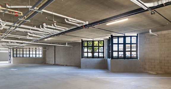 A large, empty industrial space with concrete floors and exposed ceiling pipes.
