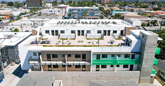 A large white building with a green stripe on the side is surrounded by other buildings.
