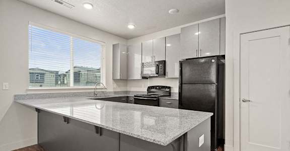 A kitchen with a black refrigerator and a granite countertop.
