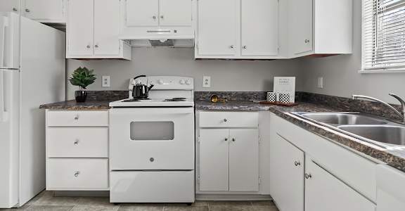 A white kitchen with a stove, sink, and cabinets.