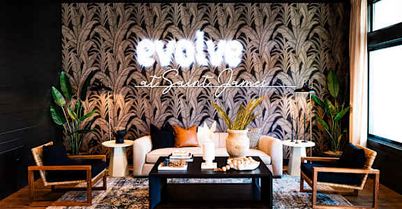 A living room with a large sofa, two chairs, and a coffee table in front of a patterned wallpaper at Evolve St. James Apartment Homes Apartments, Southport, NC, 28461