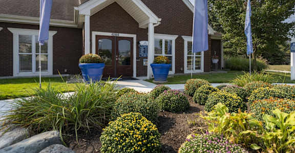 A building with a red brick facade and a white door is surrounded by a garden with various plants and flowers.