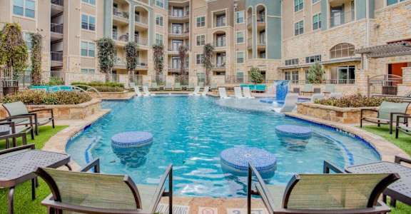 A swimming pool surrounded by lounge chairs in front of apartment buildings at The Mark at Huebner Oaks, Texas