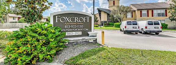 A sign for Foxcroft Apartment Homes is in front of a building and a tree.