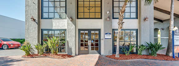 the front entrance of a building with a brick sidewalk and palm trees