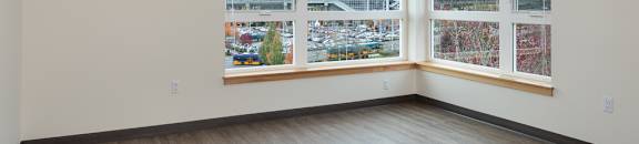 A large empty room with a view of a parking lot and trees outside.