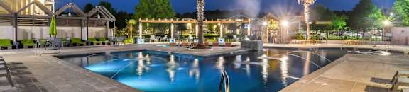 A pool area with a palm tree and lights on in the background at Reserve at Gulf Hills Apartment Homes in Mississippi 39564